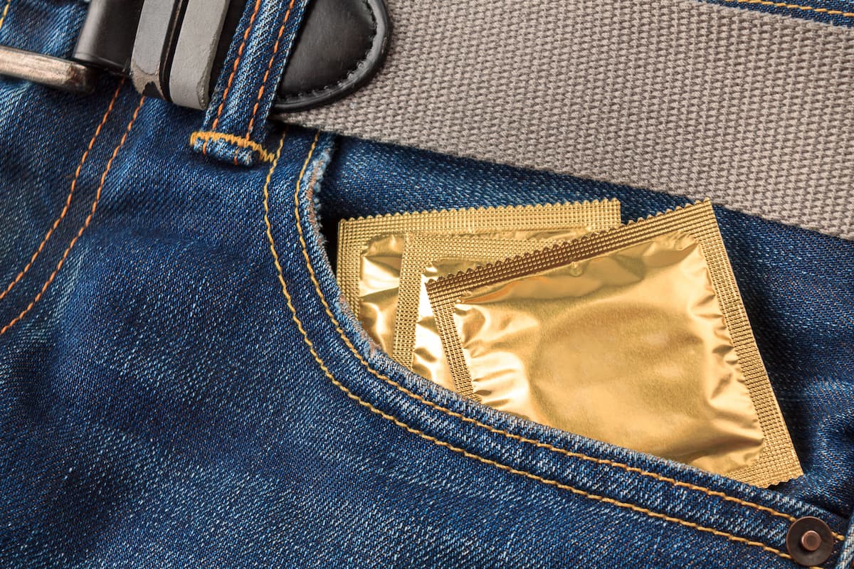 bolso de jeans azul com zíper e cinto cinza abriga dois preservativos embalados em papel dourado que protegem contra herpes genital