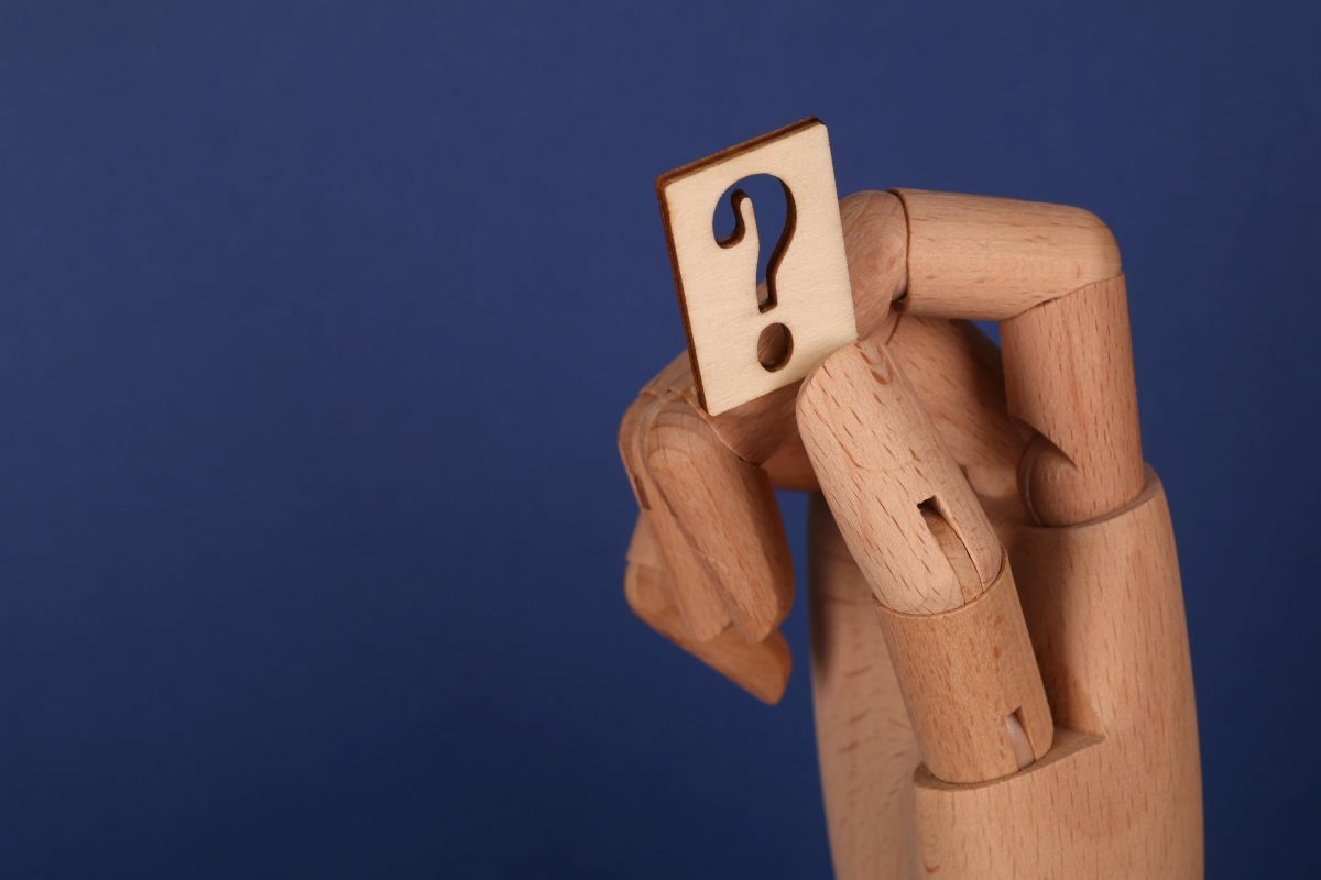 wooden hand on a blue background holding a small wooden board with a question mark