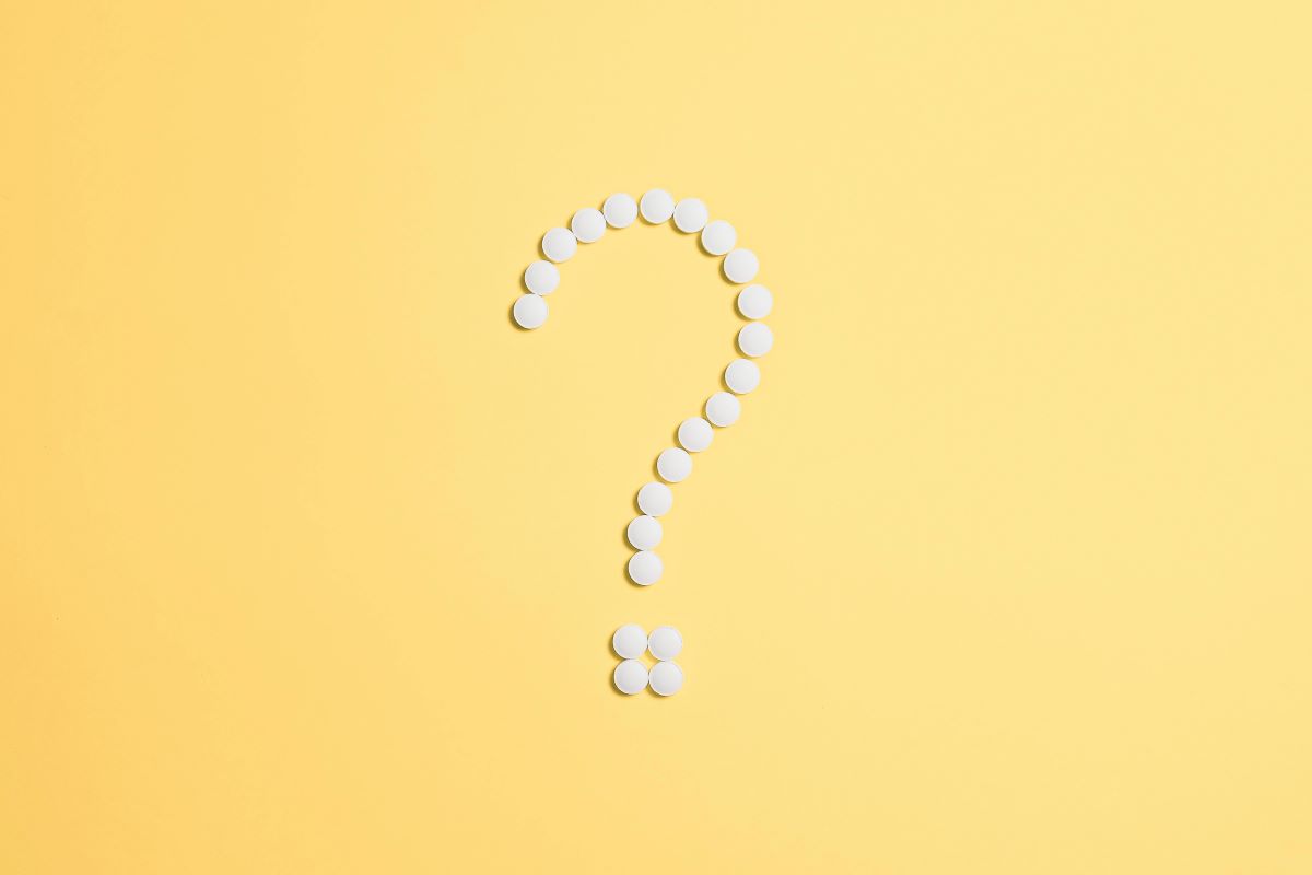 Un signo de interrogación formado por pastillas sobre una superficie amarilla.