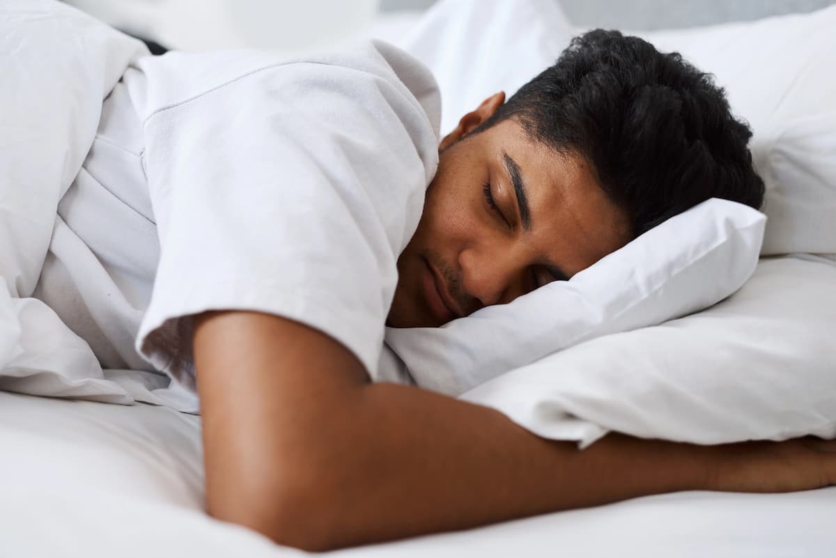Man sleeping on his side under white sheets, illustrating whether melatonin causes impotence