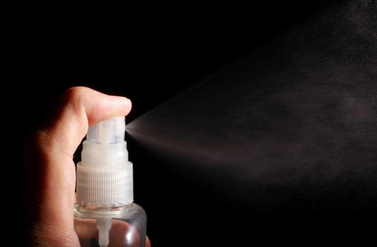 Spray para ereção sendo aplicado, com fundo preto e embalagem branca e transparente