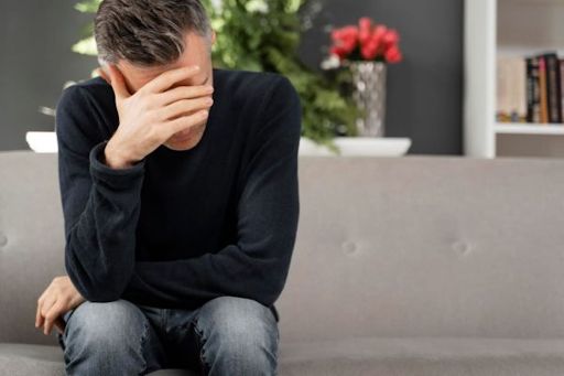 Homem sentado em um sofá com uma das mãos sobre os olhos para expressar preocupação