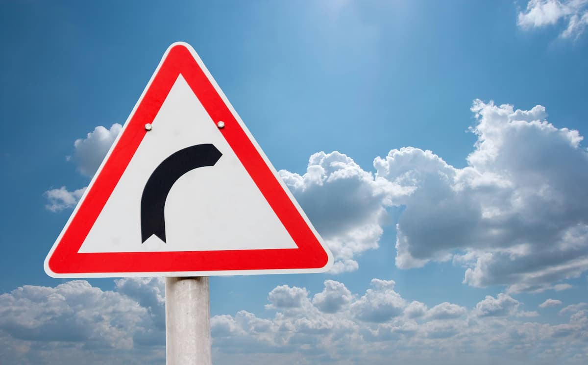 Placa de advertência com contorno vermelho e símbolo preto indicando uma curva à direita, sob céu azul, representando Técnica Egydio vs. tratamentos alternativos para Peyronie