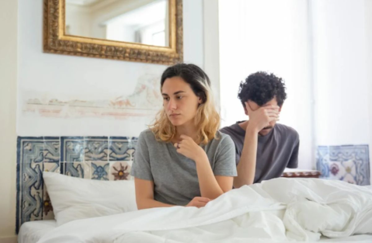 Couple in bed showing frustration, man with hands on head.