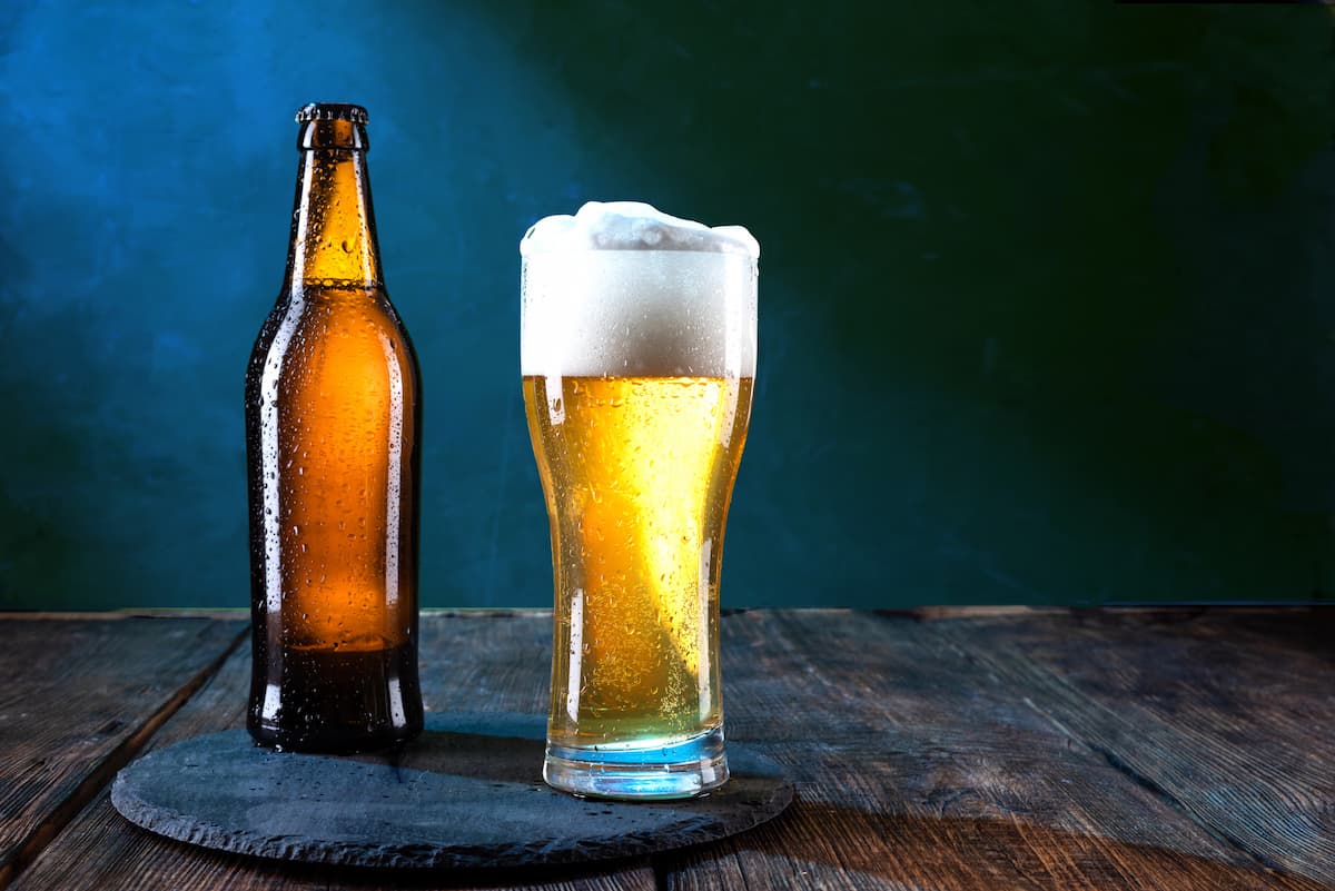 Garrafa e copo de cerveja com gotas de condensação em fundo escuro representando cerveja e saúde da próstata