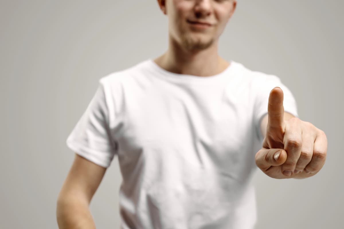 man in white T-shirt, face partially out of frame, pointing finger forward symbolizing the penile implant touch