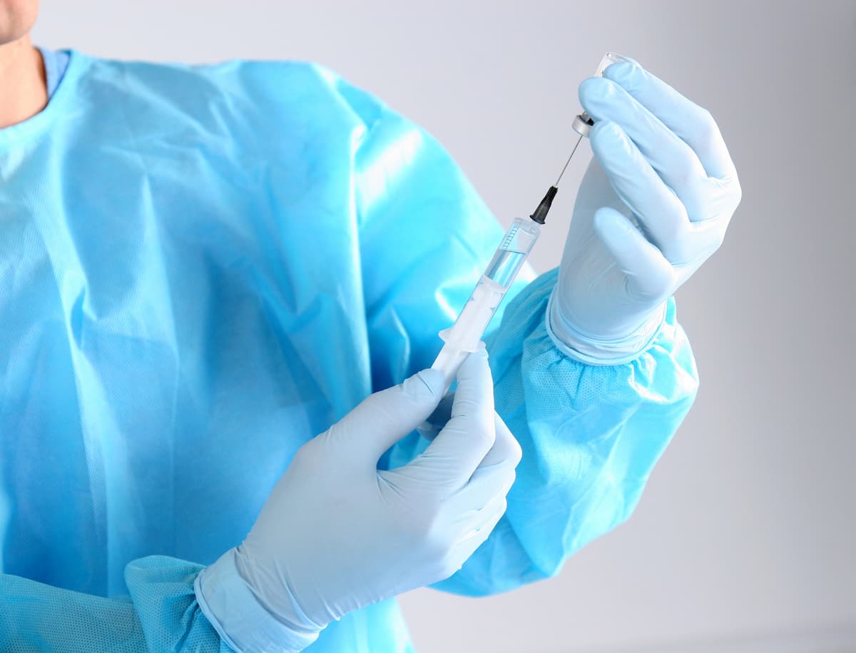 Profissional da saúde com roupa cirúrgica azul e luva azul manipulando seringa com preenchimento para harmonização peniana