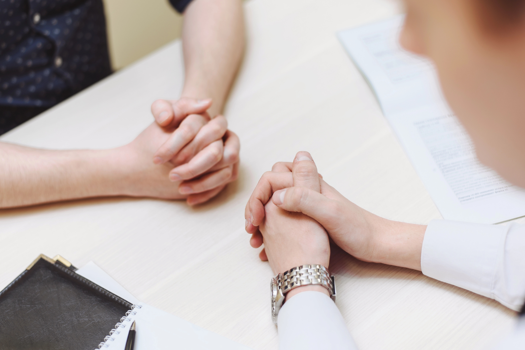 Man and woman sitting face to face at a table with their hands resting and intertwined on the surface, talking about how to talk to your partner about sexual problems