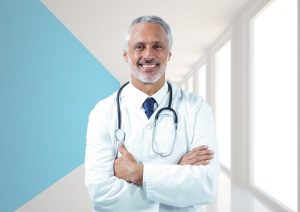 Médico com cabelo e barba grisalhos com os braços cruzados usando jaleco branco, gravata escura e estetoscópio