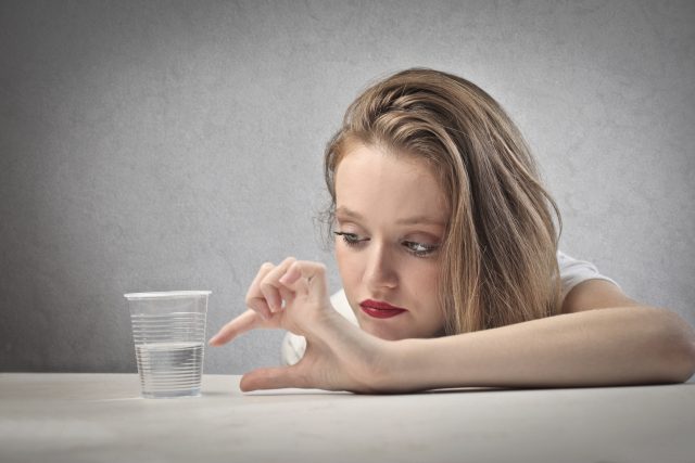 Mulher pessimista olhando para um copo meio vazio. Representação do estudo onde concluiu que homens pessimistas são mais propensos à ter dificuldade de ereção.