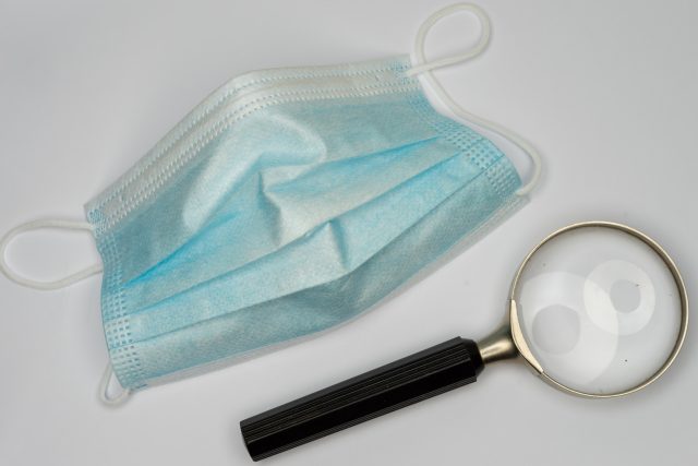 Superfície branca com máscara cirúrgica e lupa representando como é feita a cirurgia de faloplastia para aumentar o pênis