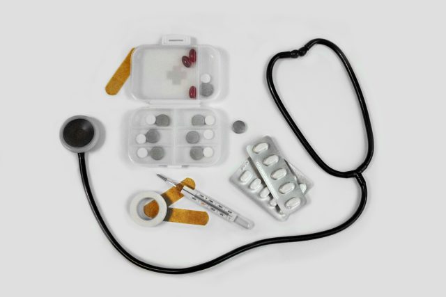 Superfície branca com caixa de remédios, blíster de remédio, band-aid, curativo, injeção e estetoscópio que ajudam como tratar a fibrose