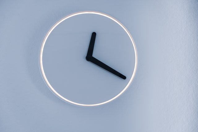 Fundo cinza azulado com relógio sem números branco e ponteiros preto marcando uma hora e vinte minutos simbolizando a relação entre corpos cavernosos e priapismo por mais de três horas
