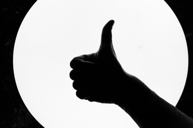 Imagem em preto e branco com uma parte do braço e mão com o polegar levantado simbolizando uma boa função erétil